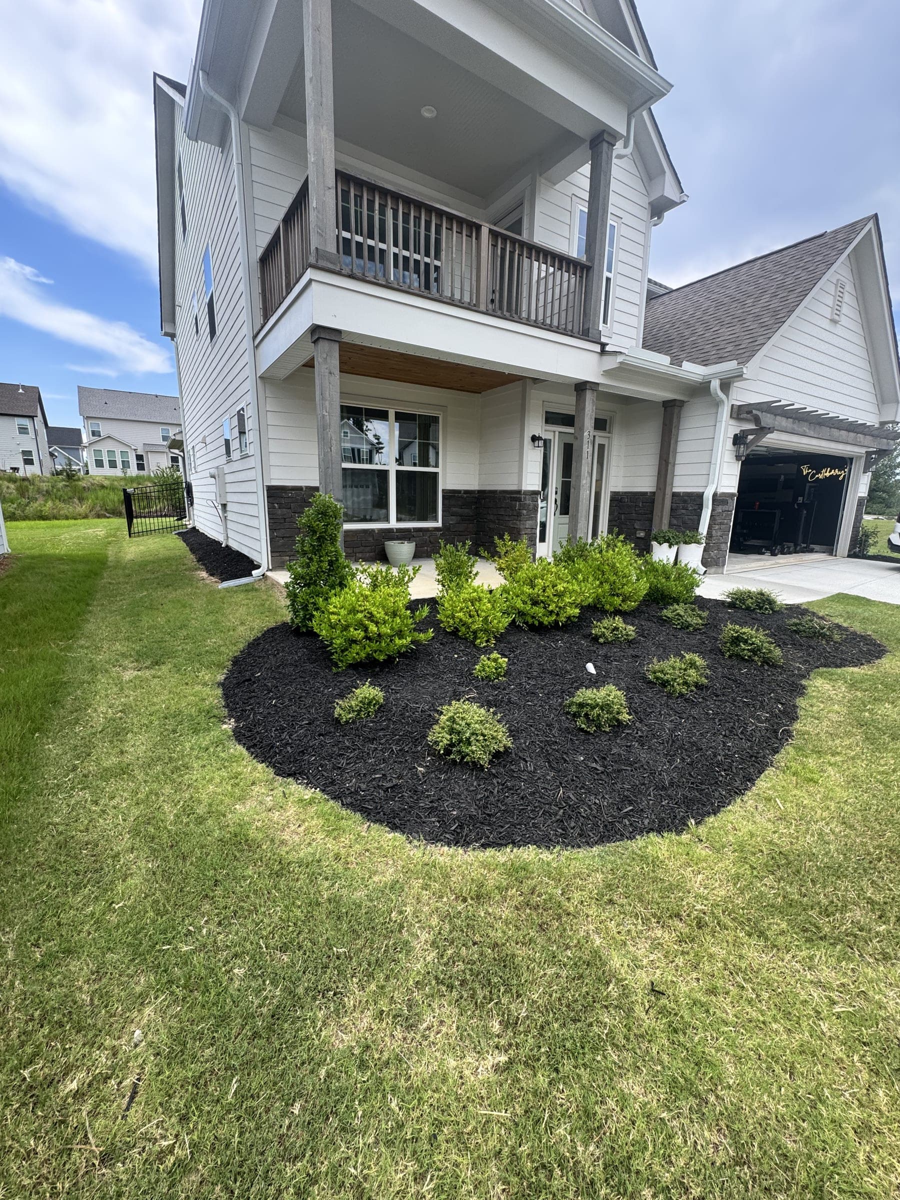 Mulched planting bed with shrubs in front of a two-story home